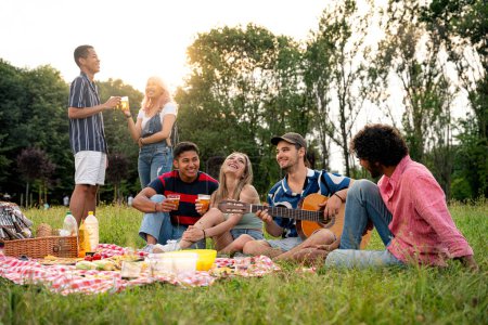 Foto de Grupo de adolescentes multiétnicos que pasan tiempo al aire libre en un picnic en el parque. Concepto sobre generación z, estilo de vida y amistad - Imagen libre de derechos