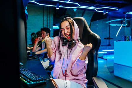 Photo for Beautiful young asian woman playing videogames in a internet cafe - Videogamer having fun playing e-sports at computer videogame console - Royalty Free Image