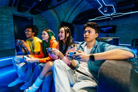 Photo for Multiethnic group of young friends playing videogames at home sitting on the sofa - Videogamers having fun playing e-sports at computer videogame console - Royalty Free Image