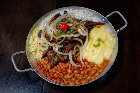 Foto de Olla de esmalte con frijoles, arroz, puré de papas, carne frita y rodajas de cebolla - Imagen libre de derechos