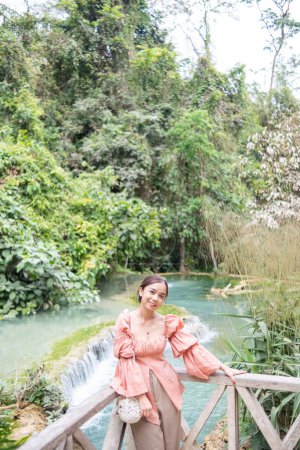 Photo for Young Asian woman standing on the wooden walkway in the Kuang Si Waterfall Popular attractions of Lung Prabang, Laos - Royalty Free Image