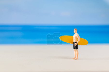 Les gens miniatures homme en maillot de bain, et tenant une planche de surf jaune sur la plage et copier l'espace pour le texte