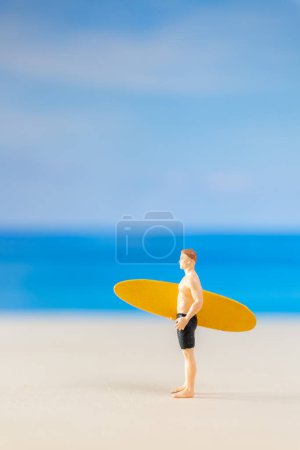 Les gens miniatures homme en maillot de bain, et tenant une planche de surf jaune sur la plage et copier l'espace pour le texte
