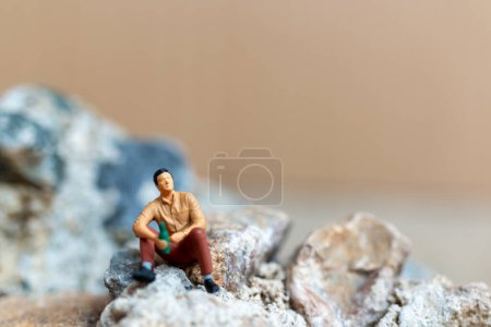Miniaturmenschen, ein junger Mann nippt am Bier, während er auf dem Felsen sitzt