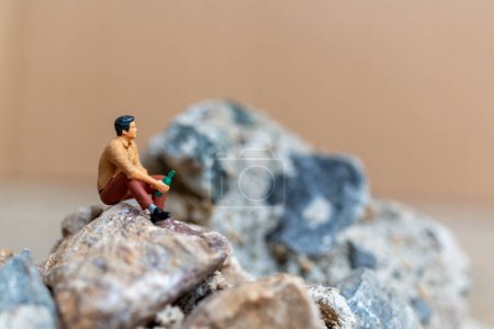 Photo for Miniature people , A young man sipping beer while sitting on the rock - Royalty Free Image
