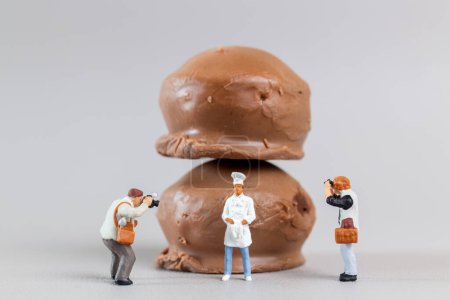 Miniaturmenschen, professioneller Konditor macht leckeres Schokoladendessert auf grauem Hintergrund, Konzept zum Weltschokoladentag