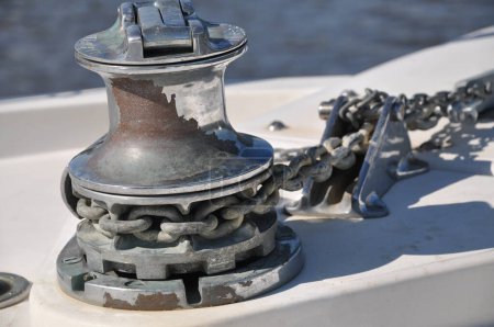 Photo for Metallic rusty anchor windlass on a white boat at the sea. Anchor is pulled up with the winch and chain. Metal looks shiny in the sun on a summer day, fun family boat ride. - Royalty Free Image