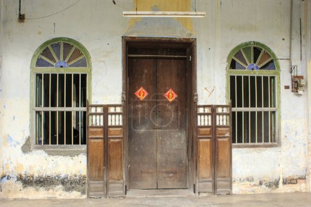 Téléchargez les photos : Ipoh, Perak, Malaisie - Novembre 2012 : La façade d'une ancienne maison vintage avec une porte en bois et des fenêtres latérales dans la ville abandonnée de Papan près d'Ipoh. - en image libre de droit