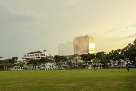 Téléchargez les photos : Georgetown, Penang, Malaisie - Novembre 2012 : Herbe verte sur un terrain de jeu avec un bâtiment moderne façonné en verre au crépuscule à George Town, Penang. - en image libre de droit