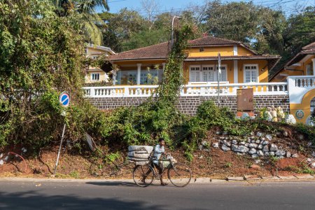 Photo for Panjim, Goa, India - January 2023: An Indian man walking with his bicycle past an old grand Portuguese era house in the Altinho area of Panaji. - Royalty Free Image