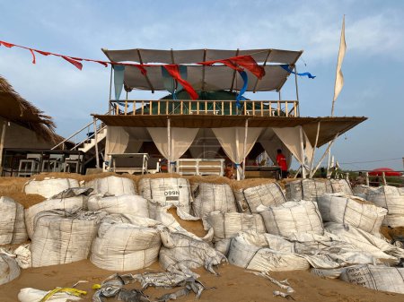 Téléchargez les photos : Candolim, Goa, Inde - Janvier 2023 : De grands sacs de sable empilés à l'extérieur pour protéger une cabane de restaurant en bord de mer afin de prévenir l'érosion côtière à marée haute. - en image libre de droit