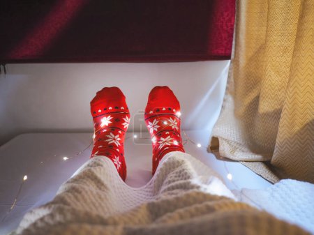 Téléchargez les photos : Touriste chaussettes rouges avec motif de Noël selfie pieds sur le lit à la capsule de l'hôtel. Joyeuses vacances sur le concept de vacances X'mas. - en image libre de droit