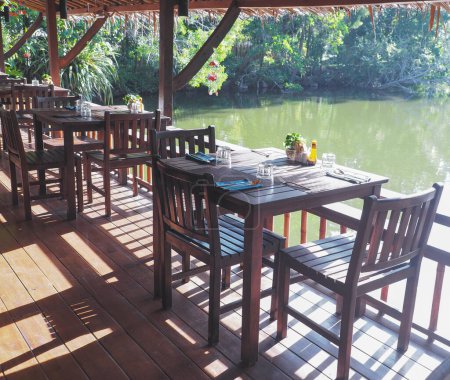 Wooden chairs and tables preparation set nearby the lake at natural restaurant. Vintage cafe decoration.