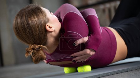 Una chica masajea el punto desencadenante de su espalda con bolas mientras está acostada en una esterilla de yoga. El concepto de liberación miofascial, auto-masaje.