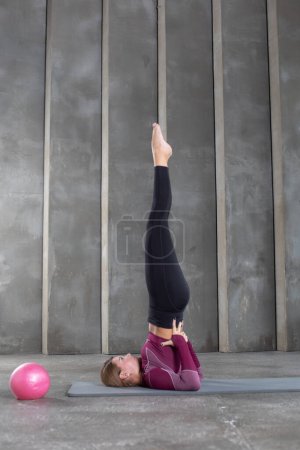 Photo for A sporty woman stands in a rack with support on her shoulders. Attractive woman practicing yoga, Salamba Sarvangasana pose. Yoga and Pilates instructor. - Royalty Free Image