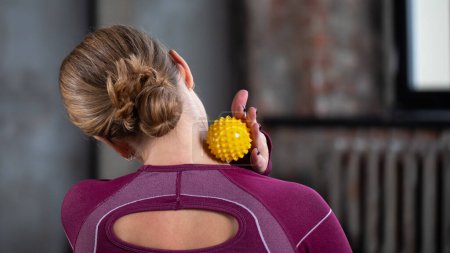 The athlete does a relaxing massage of the neck and back with the help of a prickly rubber ball. The concept of self-massage, physiotherapy.