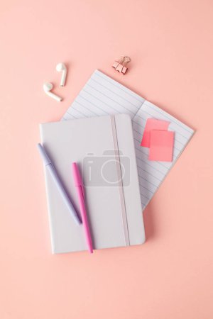 Bloc-notes, stylos et écouteurs sans fil sur fond rose. Le concept d'apprentissage en ligne, ordinateur de bureau.