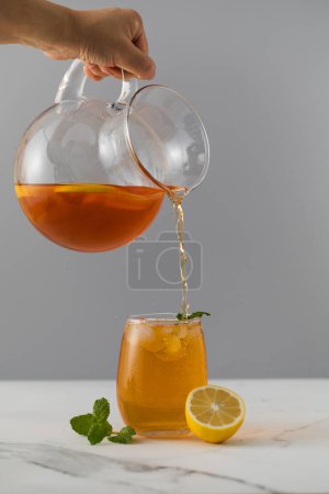 Una mujer vierte té helado con limón de una jarra en un vaso. Bebidas refrescantes verano.