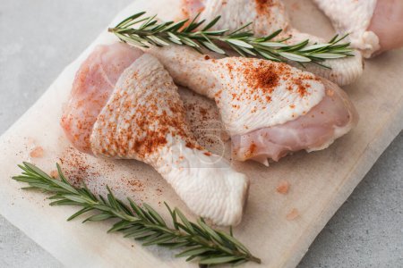 Photo for Raw chicken legs with spices and rosemary sprigs on a wooden cutting board. Farm products - Royalty Free Image