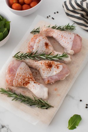 Photo for Raw chicken legs with spices and rosemary sprigs on a wooden cutting board. Farm products - Royalty Free Image