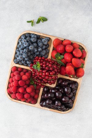 Photo for Assorted ripe and juicy berries on a wooden menagerie on a gray table. The concept of berry picking, vitamins in berries. - Royalty Free Image