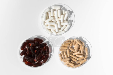Téléchargez les photos : Diverses vitamines et compléments alimentaires dans de petites assiettes médicales sur fond blanc. Le concept de médecine, les médicaments. - en image libre de droit