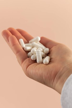 Téléchargez les photos : Capsules médicinales blanches dans une paume de femme sur fond rose, vitamines et suppléments. Le concept de médicaments. - en image libre de droit