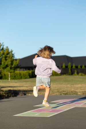 Photo for A cute girl is playing hopscotch on the asphalt in the playground. Active leisure for children. The concept of a happy childhood. - Royalty Free Image