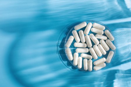 White medicinal capsules, vitamins or dietary supplements in close-up on a blue background. The concept of medicine. Copy space