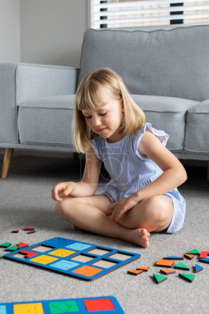 Foto de Una linda chica está jugando un juego de madera lógica en el suelo en la habitación. Juguete educativo de madera para niños. Desarrollo y educación infantil. - Imagen libre de derechos