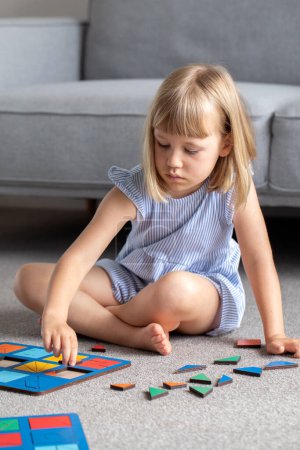 Foto de Una linda chica está jugando un juego de madera lógica en el suelo en la habitación. Juguete educativo de madera para niños. Desarrollo y educación infantil. - Imagen libre de derechos