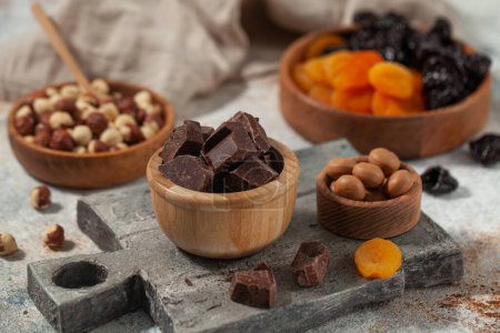 Würfel dunkler handwerklicher Schokolade. Verschiedene Nüsse, dunkle Schokolade und getrocknete Früchte auf Stein, ein Fest für die Sinne. 