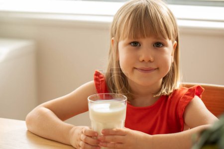 Glückliches Mädchen mit einem Glas Milch, das zu Hause ein gesundes und nahrhaftes Getränk genießt. Milchprodukte