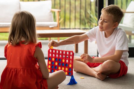 Geschwister vertieft in ein strategisches Brettspiel, das ihre Logik und Bindung verbessert. Kinder spielen Brettspiele - zu viert in einer Reihe. Logikspiel