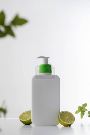Photo for A sleek white shampoo or shower gel bottle with a vibrant green pump, accented by fresh lime slices, against a pure white background. Skin care - Royalty Free Image