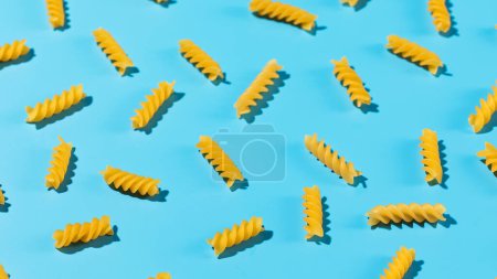 Uncooked fusilli pasta spirals scattered on a blue background in a decorative pattern, emphasizing texture and shape.