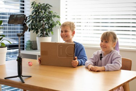 Kids recording an unboxing video for their vlog, smiling and excited as they reveal the contents of the box, creating fun and engaging content.