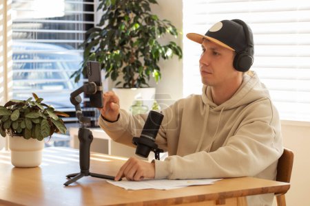 Man adjusts smartphone on gimbal for podcast recording in a home setup. Online training