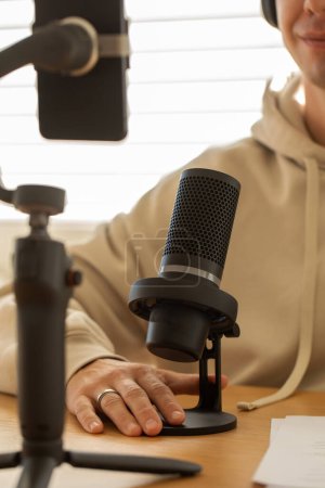 Ein Smartphone auf einem Gimbal mit Mikrofon, für Content Creator. Podcast-Mikrofonaufbau auf einem Holztisch, warmes Licht. Das Konzept der Aufzeichnung eines Podcasts, Bloggen