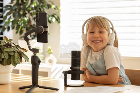 Junges Mädchen mit Kopfhörern, die während einer Podcast-Session lächeln, ausgestattet mit Mikrofon und Smartphone. Das Konzept des Bloggens und Podcasts.