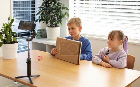 Niños grabando un video de unboxing para su vlog, sonriendo y emocionados mientras revelan el contenido de la caja, creando contenido divertido y atractivo.