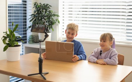 Kids recording an unboxing video for their vlog, smiling and excited as they reveal the contents of the box, creating fun and engaging content.