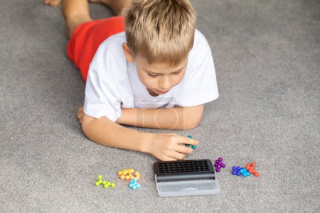 Garçon concentré profondément engagé dans la résolution d'un puzzle logique coloré, l'amélioration de ses compétences cognitives. Développement de l'enfant.
