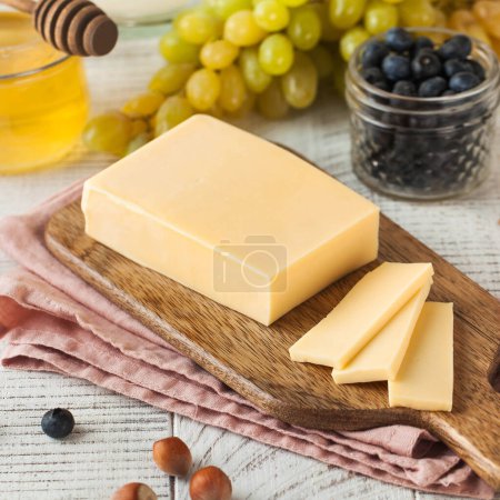 Un morceau appétissant de fromage naturel sur une planche de bois avec du miel et des raisins. Fromage à la crème. Produits laitiers.