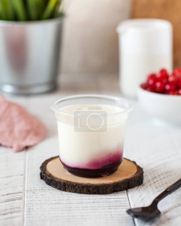 Delicate panna cotta or Greek yogurt with berry jam in a transparent plastic cup on a wooden stand in a rustic style