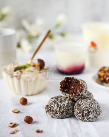 Chocolate candies covered with coconut flakes against dairy desserts on table. Healthy cocoa bonbons pile with nuts. Organic sweets for diet vertical shot