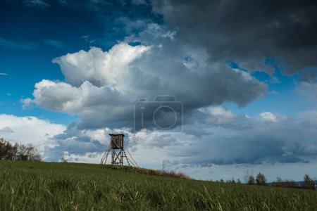 Téléchargez les photos : Chasseur de bois siège haut sur le terrain avec de lourds nuages sur le sol plat - en image libre de droit