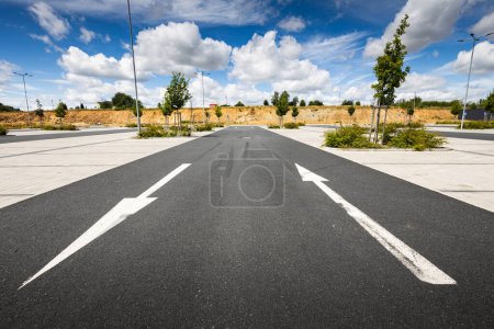 Téléchargez les photos : Route asphaltée vide avec des flèches blanches et des nuages sur fond bleu ciel - en image libre de droit