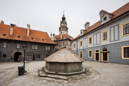 Foto de Patio vacío con cubierta de fuente de madera en primer plano, edificios del castillo y torre en el fondo, Cesky Krumlov, República Checa, Europa - Imagen libre de derechos