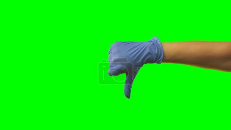 Téléchargez les photos : Main de femme en gant bleu latex montre pouces vers le bas. Bras de médecin dans des gants médicaux de protection signe gestuel négatif, mauvais, non recommandé. Gros plan sur fond vert - en image libre de droit